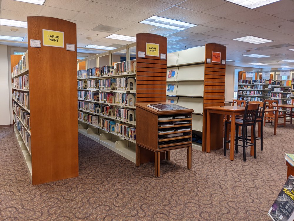 Shelves of large print and fiction at the Main Library, with reading tables beyond them.