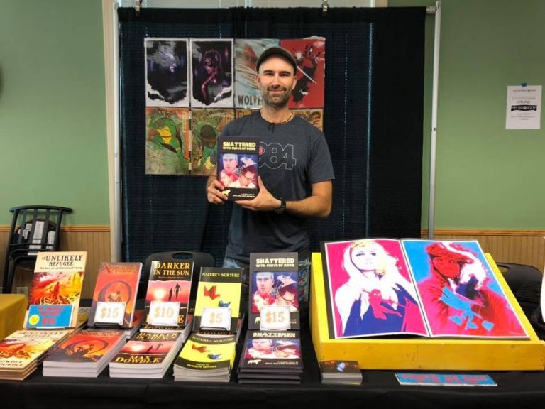 An author showing his book to a visitor at the Local Author Book Fair.