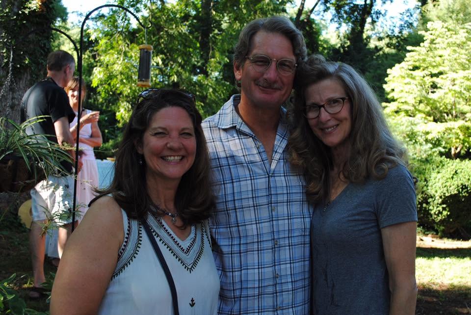 Three smiling supporters at an outdoor Friends gathering under summer trees