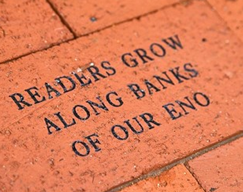 Close-up of an engraved clay brick in the library walkway reading Readers Grow Along Banks of Our Eno